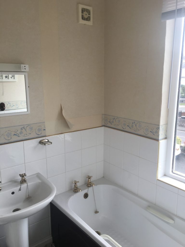 Bathroom with white tiles halfway up the wall and a white bath and sink with gold taps