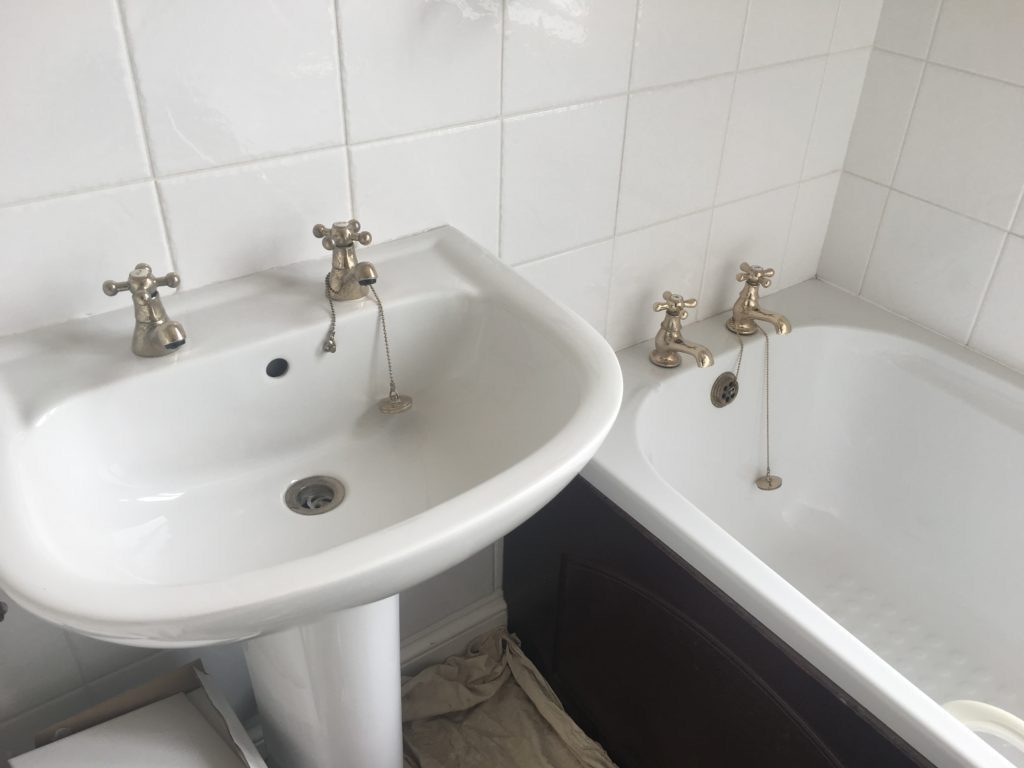 White sink and bath with gold taps against a white tiled wall