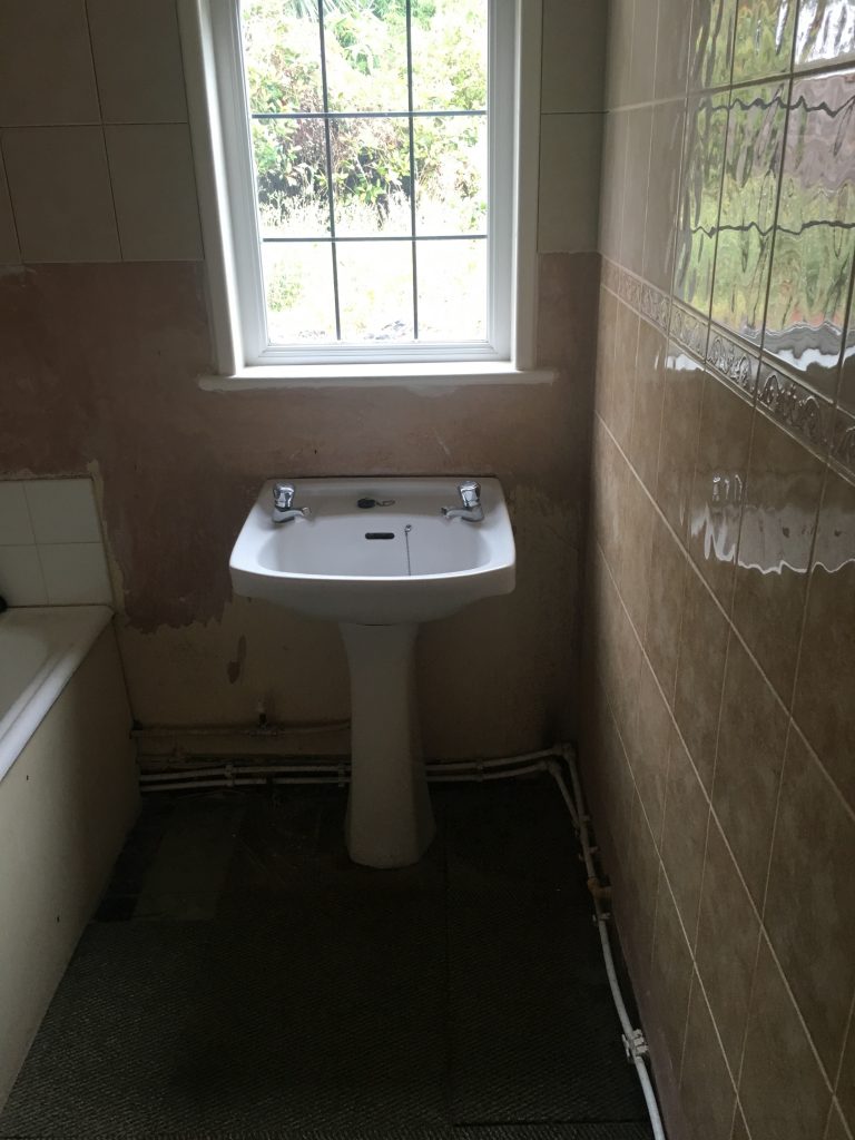White sink underneath window surrounded by clay coloured tiled walls