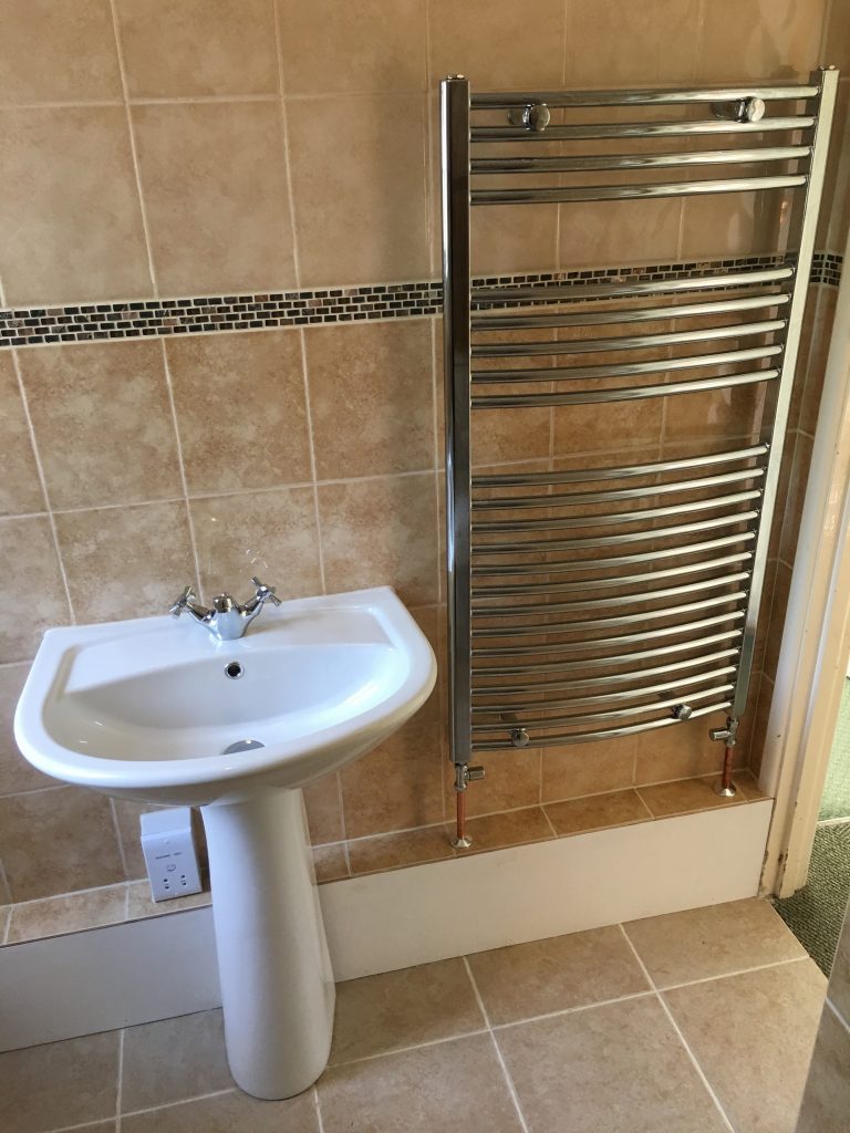White sink next to towel radiator against clay tiled walls with mosaic trim