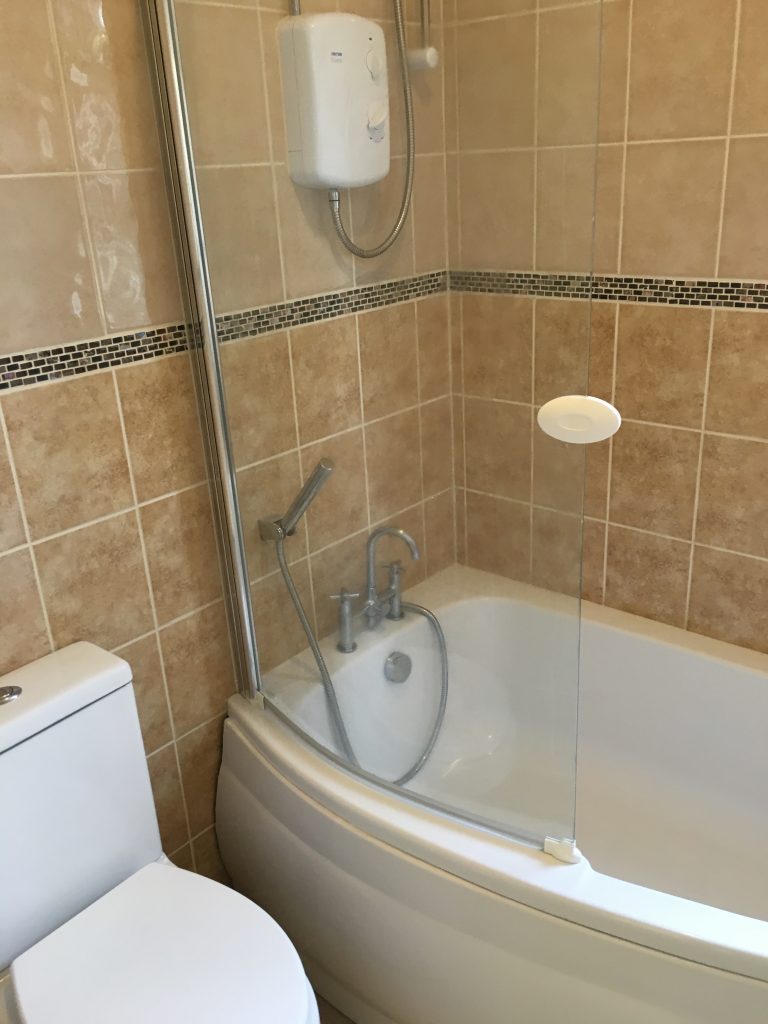 Bath with shower tap and overhead shower next to white toilet