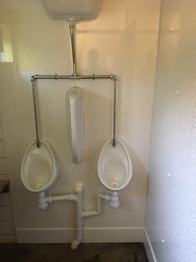 Two urinals with privacy screen surrounded by white speckled wipeable walls