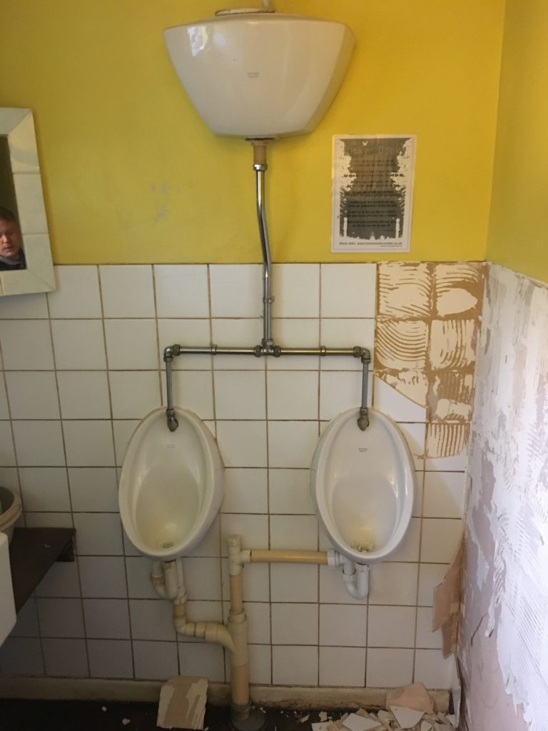 Two urinals surrounded by broken white wall tiles 