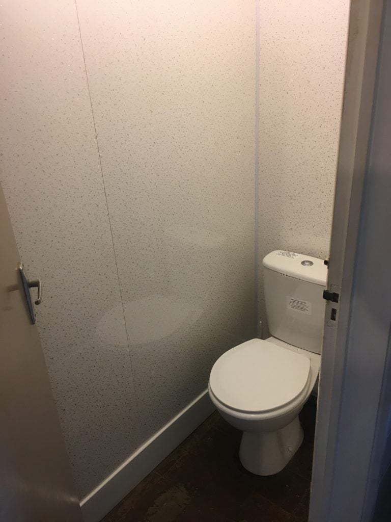 Office toilet cubicle with white toilet surrounded by white speckled wipeable walls
