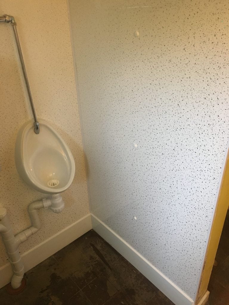 Urinals surrounded by white with black speckles wipeable wall